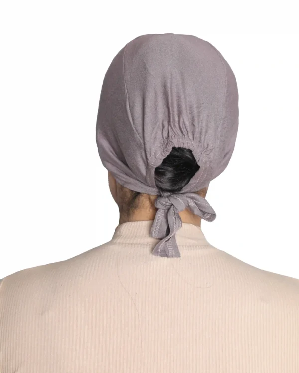 A woman models a Chic Grey Turban Cap for Women, viewed from the side and looking down, highlighting the gentle pleating and single line of stitching above the brow.