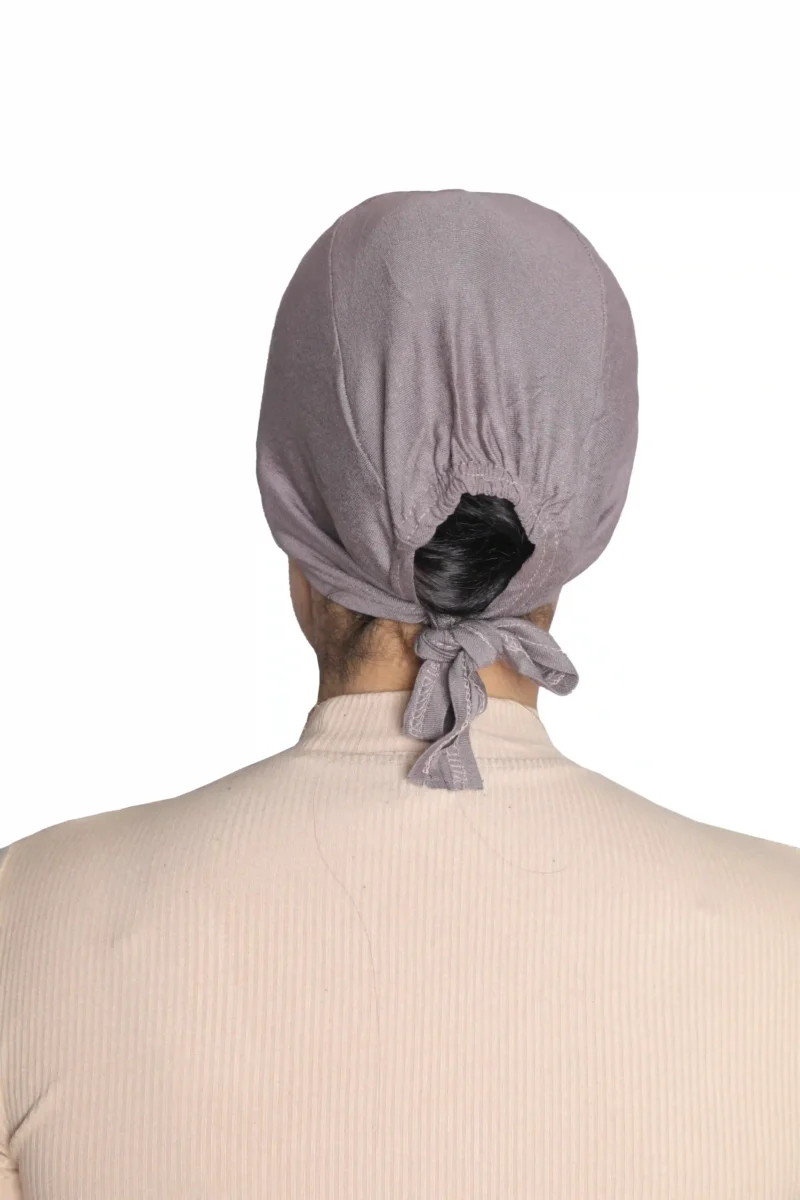 A woman models a Chic Grey Turban Cap for Women, viewed from the side and looking down, highlighting the gentle pleating and single line of stitching above the brow.